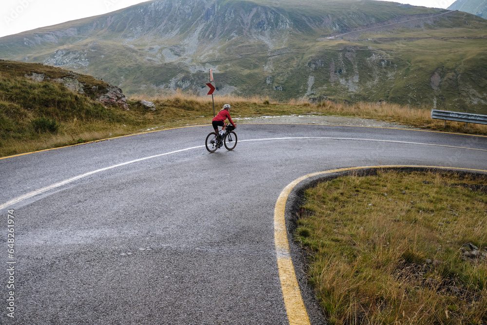 Female cyclist in bike packing tour.Bikepacking travel.Female cyclist is riding through foggy mountain landscape.Adventure cycling concept. Woman cycling in the nature.Transalpina road.Parâng Mountain Female cyclist in bike packing tour.Bikepacking travel.Female cyclist is riding through foggy mountain landscape.Adventure cycling concept. Woman cycling in the nature.Transalpina road.Parâng Mountain