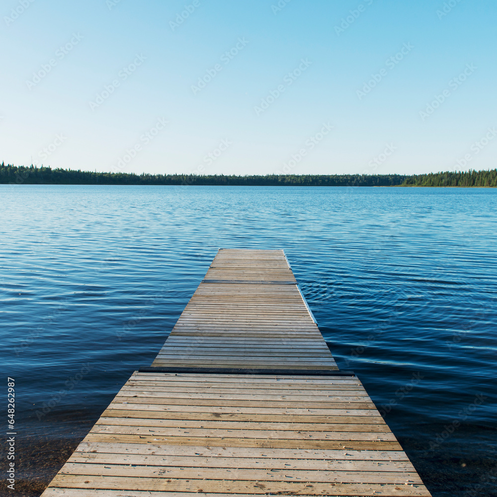 A Wooden Dock Leading Out To A Lake And Blue Sky In Riding Mountain National Park; Wasagaming, Manitoba, Canada A Wooden Dock Leading Out To A Lake And Blue Sky In Riding Mountain National Park; Wasagaming, Manitoba, Canada