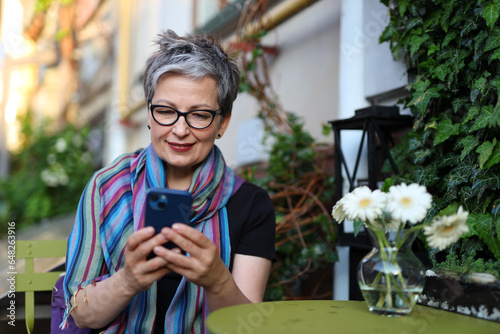 A cheerful senior woman using modern technology, her smartphone, for communication and leisure outdoors.