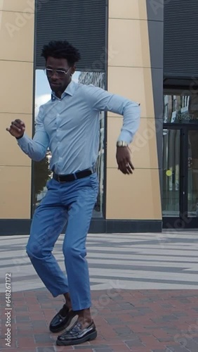 African American man dancing on city street near building, wearing formal clothes blue trousers and shirt. Handsome black male model outdoors.