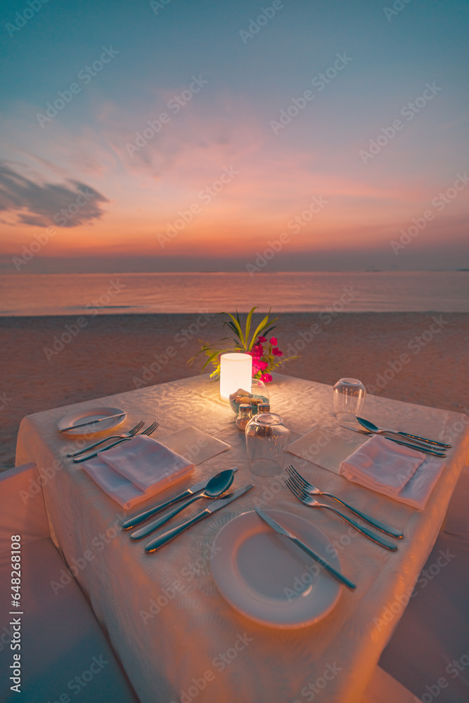 Amazing romantic dinner table on beach sand candles under sunset sky
