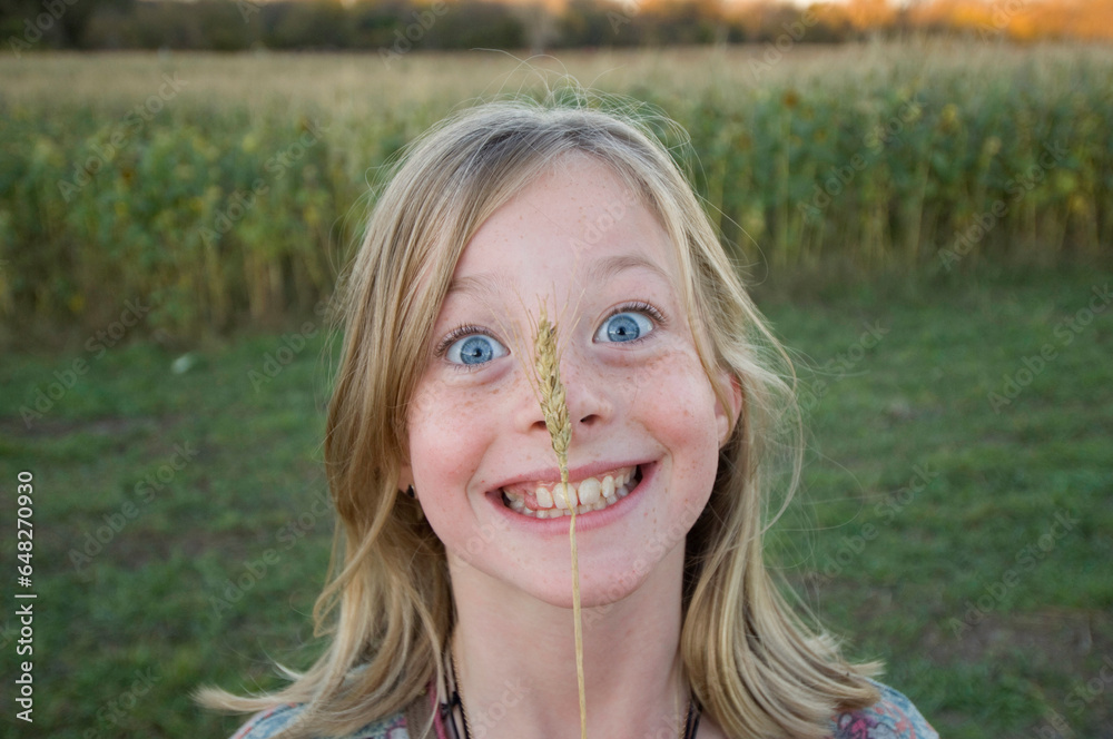 Young girl holds a piece of wheat up to her big blue eyes; Roca, Nebraska, United States of America Young girl holds a piece of wheat up to her big blue eyes; Roca, Nebraska, United States of America