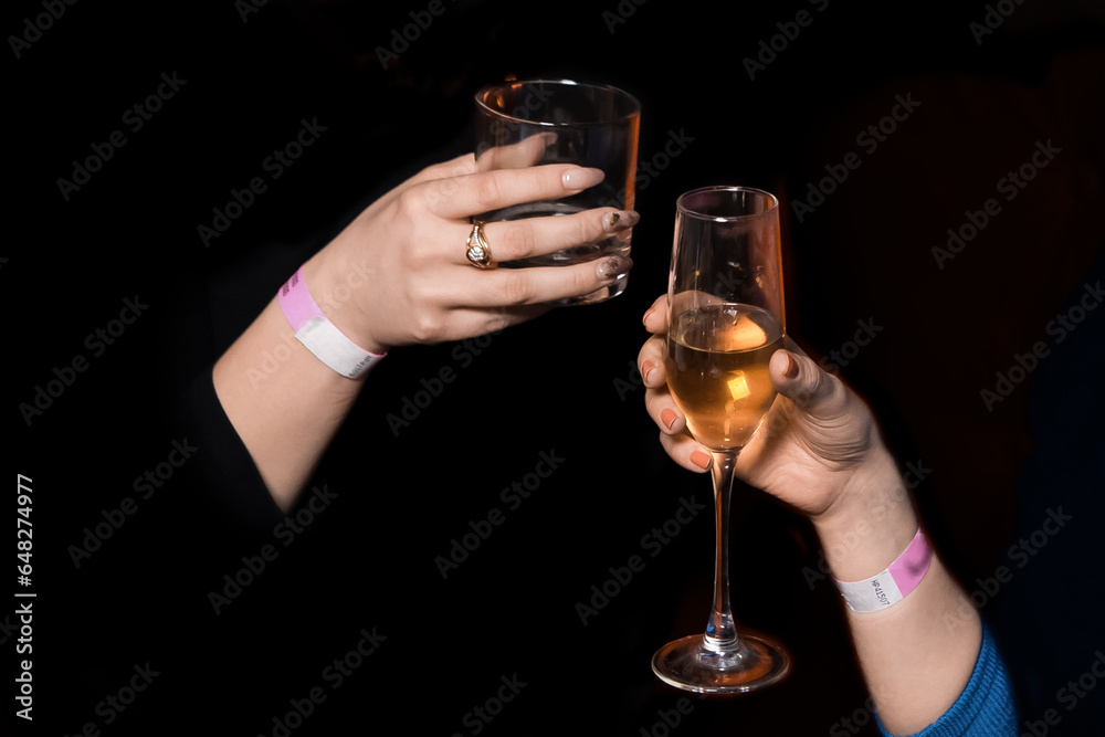 The hands of girls, friends clinking glasses of alcoholic beverages on a black background, holiday atmosphere, weekend