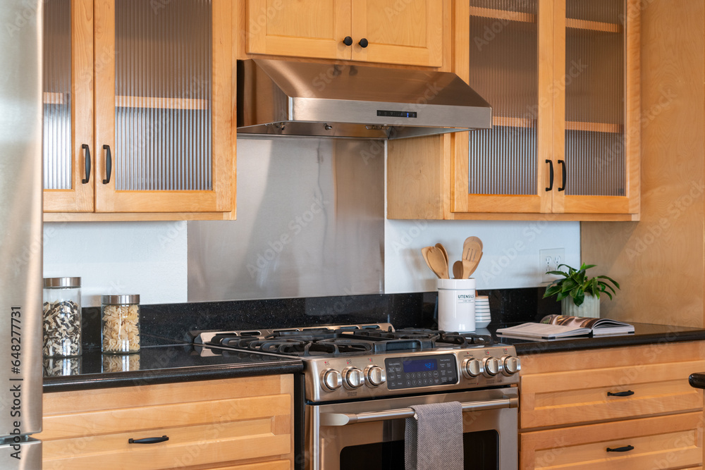 Modern kitchen details of honey wood cabinets with gas range and black counters. Modern kitchen details of honey wood cabinets with gas range and black counters.