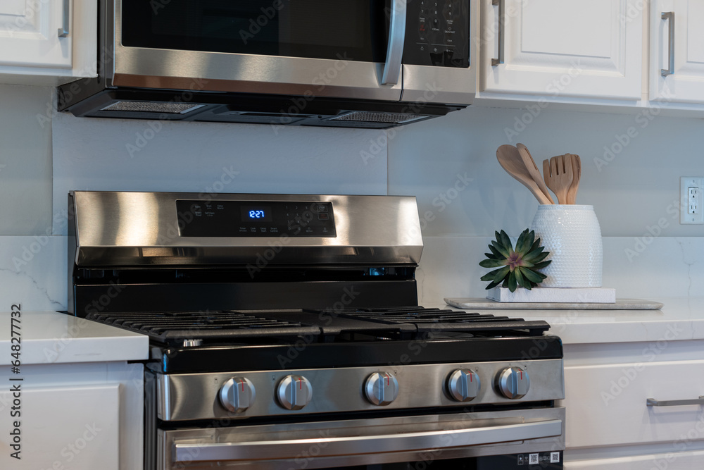 Simple kitchen details of gas stove with white ceramic jar of wood spoons and decorative plant. Simple kitchen details of gas stove with white ceramic jar of wood spoons and decorative plant.