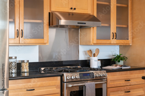 Modern kitchen details of honey wood cabinets with gas range and black counters.
