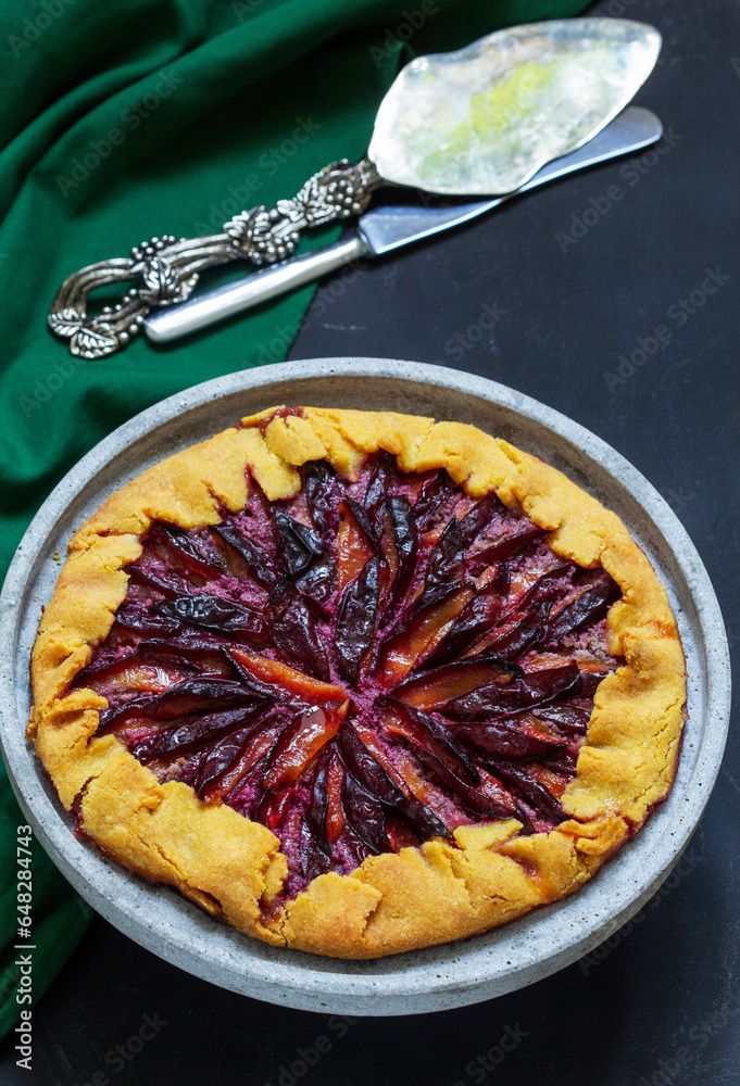 Traditional french pie galette made of corn dough with plum filling on a concrete tray.