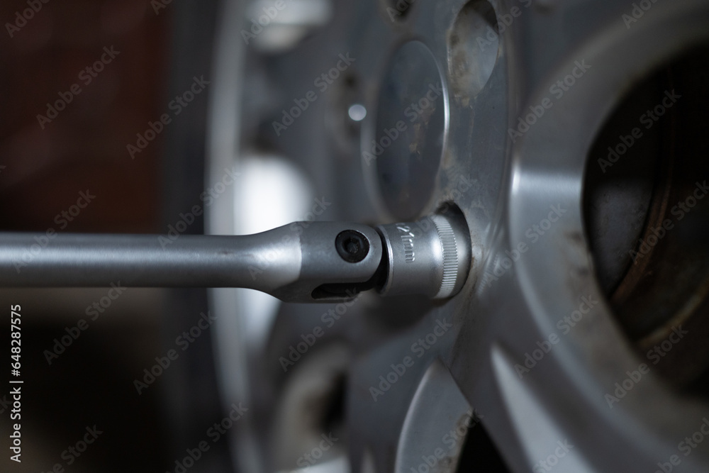 Close-up of a wrench unscrewing bolts on a wheel in a garage. A man is repairing his car in the evening in the garage. A man changes a tire on a car in a garage. Close-up of a wrench unscrewing bolts on a wheel in a garage. A man is repairing his car in the evening in the garage. A man changes a tire on a car in a garage.