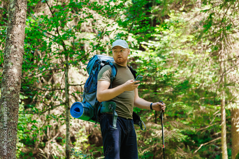 Adult man standing and browsing smartphone in green forest in daylight