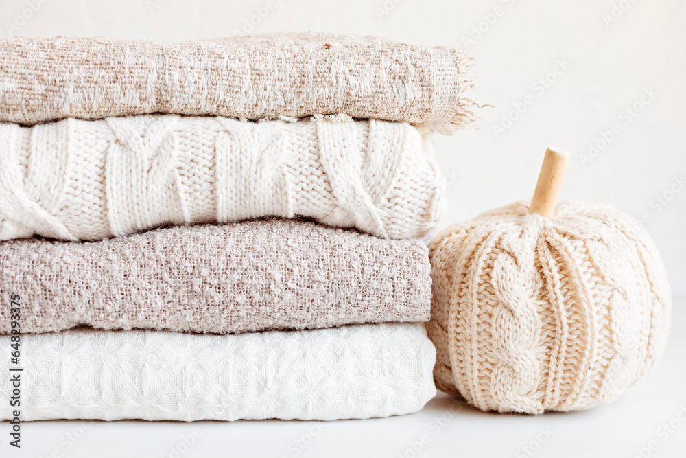Pile of cozy light knitted clothes and blankets for cold weather. Comfort organic sweaters and plaids. Hygge style idea