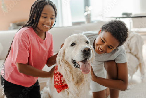 Portrait happy children, African American brother and sister stroking and playing with golden retriever dog