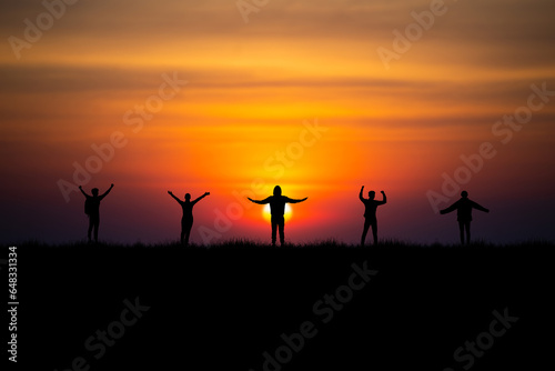 A small group of friends, both men and women, stood watching the morning sunrise on the top of a mountain and raised their arms to express their happiness at being able to travel with close friends.