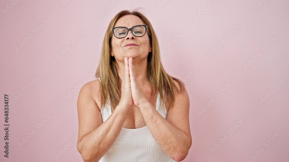 Middle age hispanic woman doing please gesture with hands together over isolated pink background