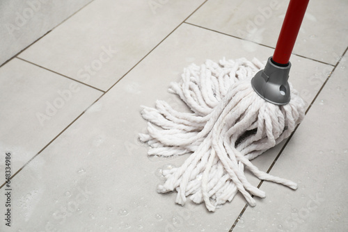 Cleaning grey tiled floor with string mop, space for text