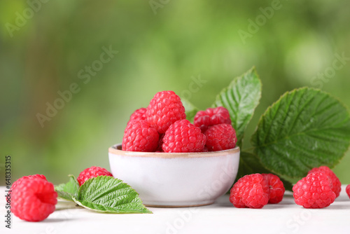 Tasty ripe raspberries and green leaves on white table outdoors