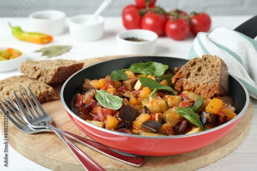 Dish with tasty ratatouille, bread and basil on wooden board