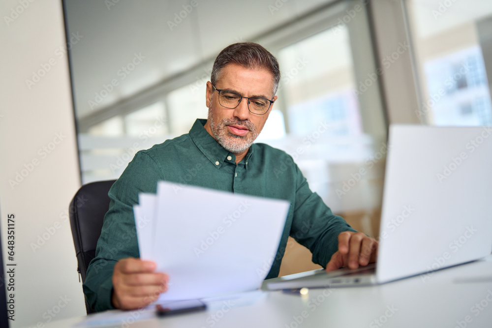 Middle aged older professional business man executive ceo accountant lawyer expert using laptop computer checking accounting legal papers financial corporate documents calculating taxes in office. Middle aged older professional business man executive ceo accountant lawyer expert using laptop computer checking accounting legal papers financial corporate documents calculating taxes in office.
