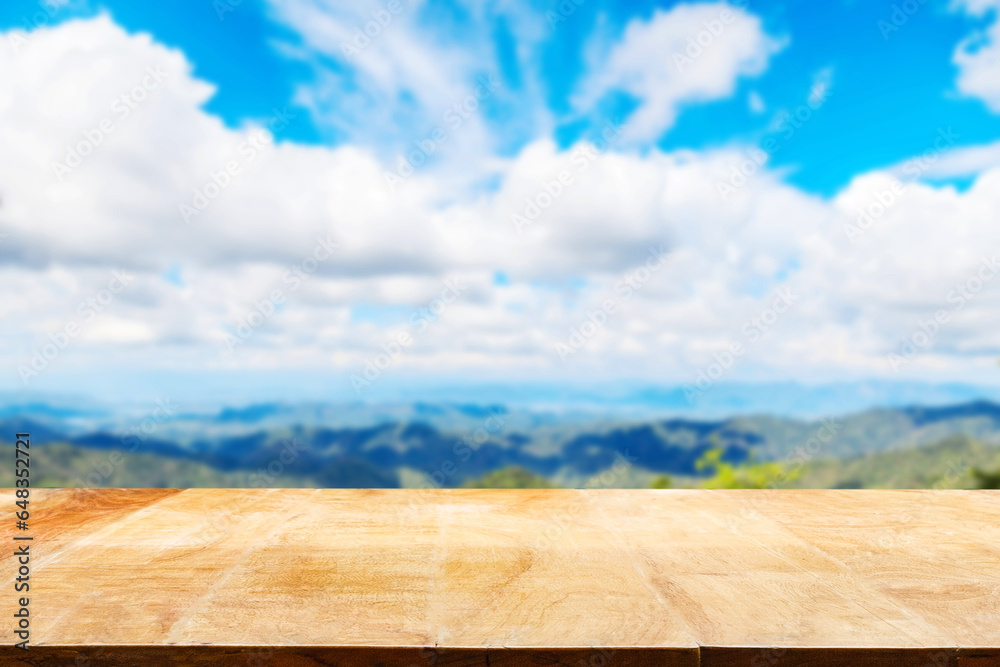 Empty old wooden table in front of blurred background of mountains, blue sky amid bright sunlight on a day..