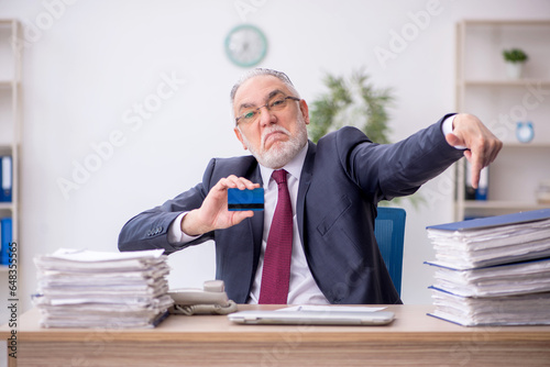 Old male employee holding credit card at workplace