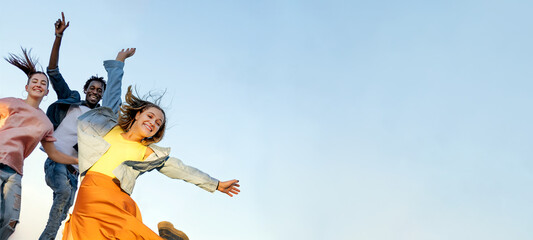 Happy friends group jumping raising arms isolated on blue sky background - Young multiracial people having fun together - Friendship and hapiness concept - Copy space