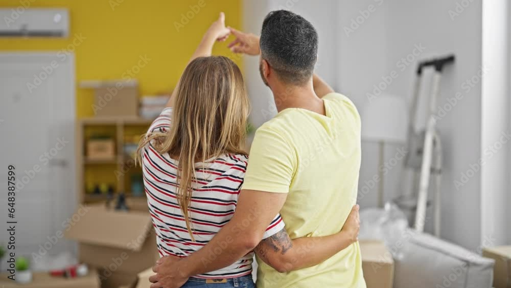 Man and woman couple hugging each other looking around standing backwards at new home Man and woman couple hugging each other looking around standing backwards at new home