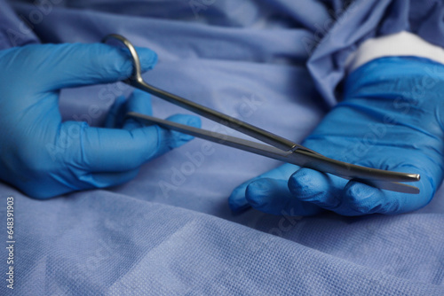 The doctor wearing blue medical gloves holds the Necrotomy Scissors or bent sharp scissors, which are the main instruments in wound debridement.