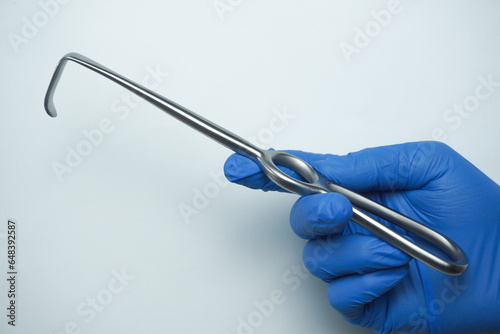 The doctor wearing blue medical gloves is holding Langenbeck, a surgical tool commonly called a hook that is used to hook the incision so that it opens wide