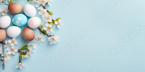 Colorful Easter eggs with spring blossom flowers on soft blue background. Top view