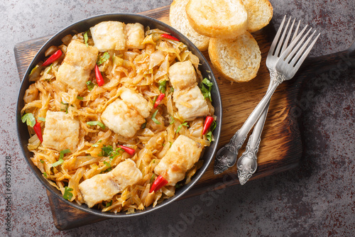 Canvas Print Stewed white cabbage with sea fish fillet, onion and chili pepper close-up in a plate served with toast on the table