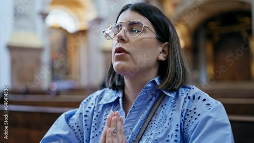 Young beautiful hispanic woman praying on a church bench at St. Karl Borromäus church photo