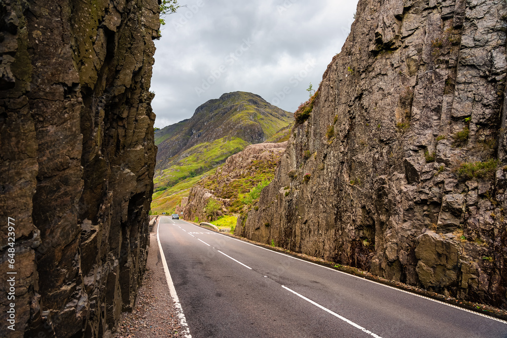 Mountain road that runs between cut rock walls in the spectacular valley of Glencoe, Scotland.