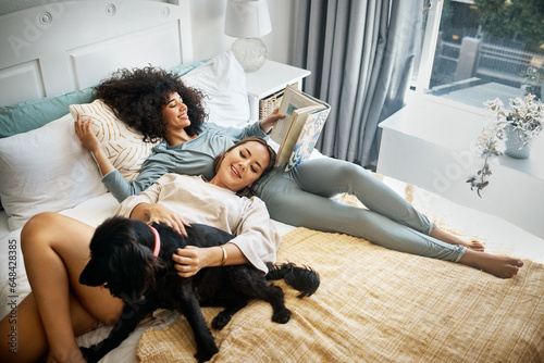 Foto Dog, bed and happy lesbian couple in home, morning and relax together reading book
