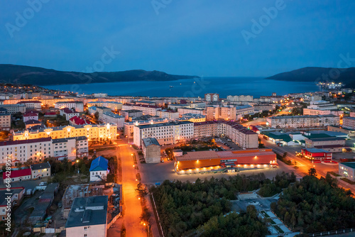 Night aerial photograph of a seaside port town. Top view of the streets and buildings. In the distance is the Nagaev Bay of the Sea of Okhotsk. City of Magadan, Magadan region, Far East of Russia.