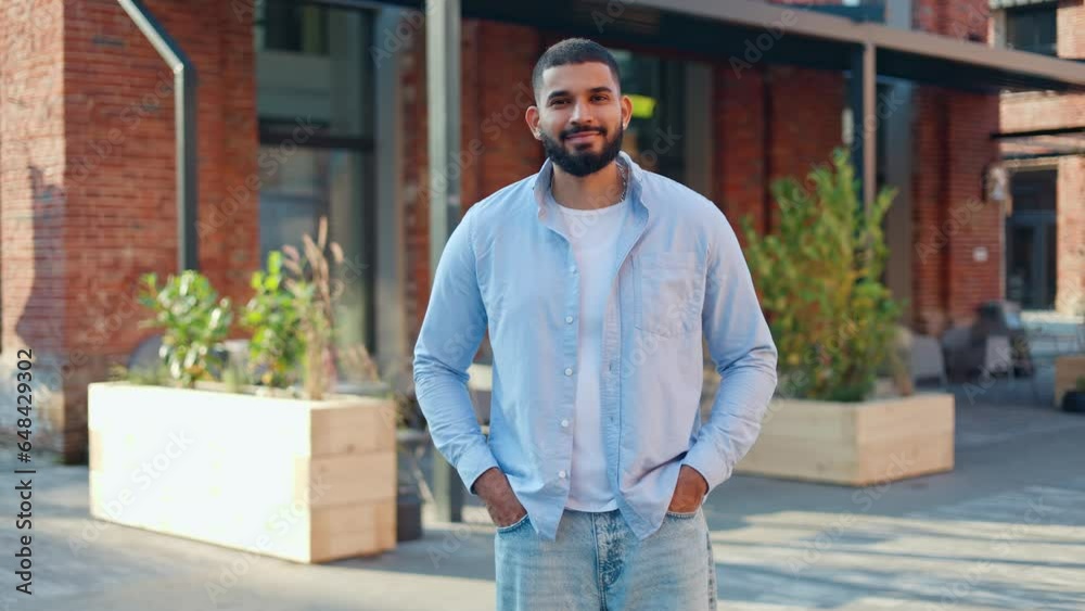 Front view of well-built man of indian ethnicity keeping hands in jeans pockets and looking sideways. Young man wearing casual clothing turning eyes at camera and making happy sincere smile. Front view of well-built man of indian ethnicity keeping hands in jeans pockets and looking sideways. Young man wearing casual clothing turning eyes at camera and making happy sincere smile.