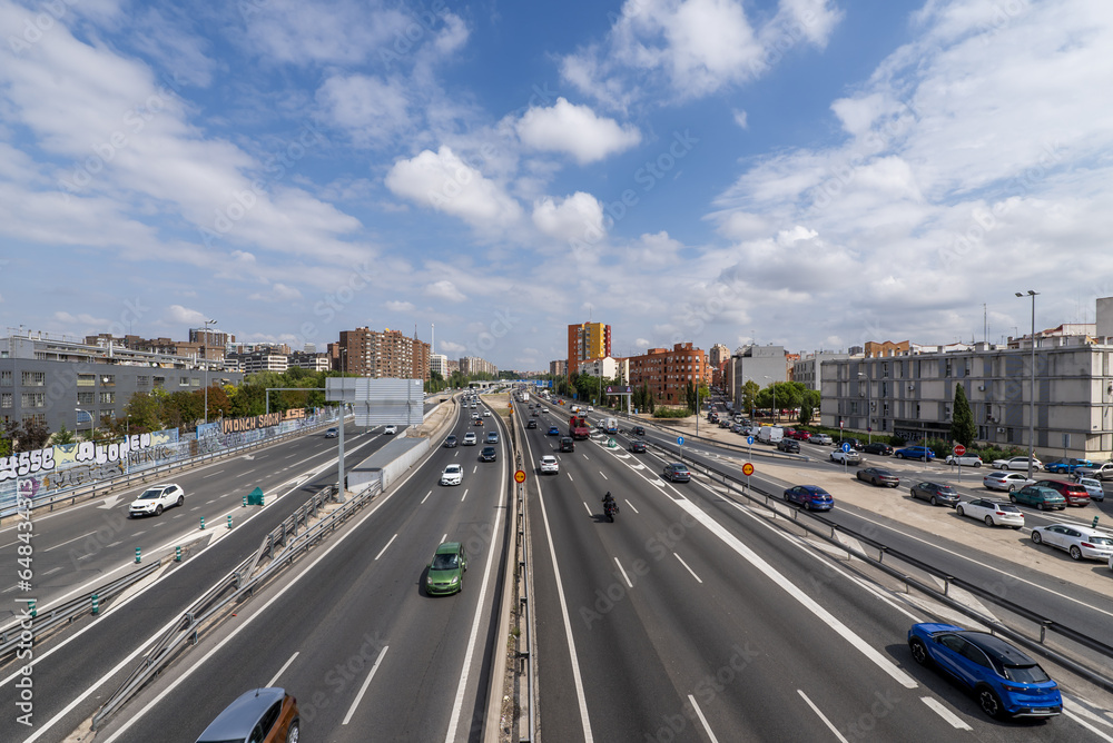 Vehicles driving on an urban road in the city of Madrid on a day with cloud-filled skies, Spain