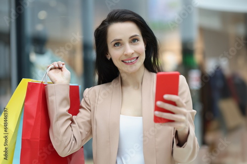 Portrait of young smiling woman holding smartphone and packages with purchases. Online shopping through mobile apps concept