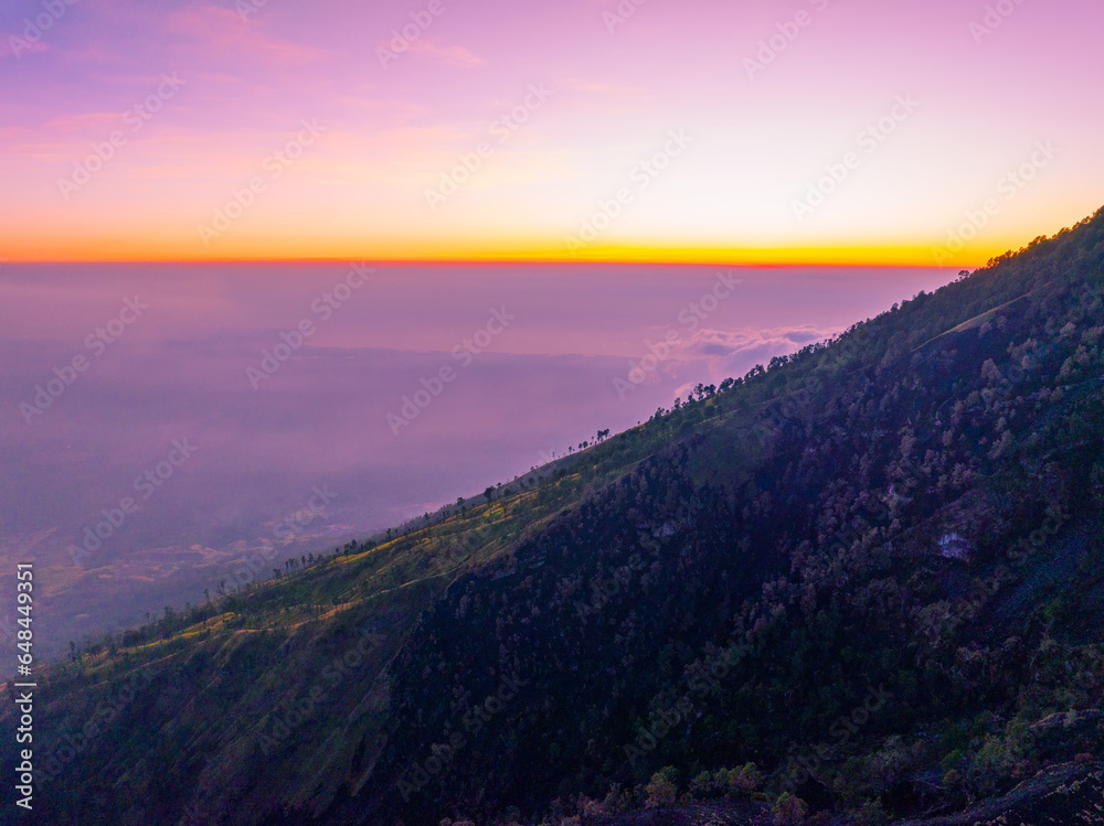 Amazing Sunset or sunrise landscape with high peaks and foggy forest under vibrant colorful sky clouds over mountains