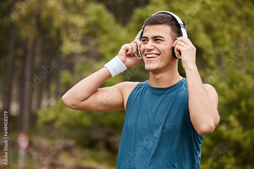 Fitness, headphones and a man outdoor listening to music or audio with wellness. Happy runner, athlete or sports person in nature park to start exercise, workout or training while streaming radio
