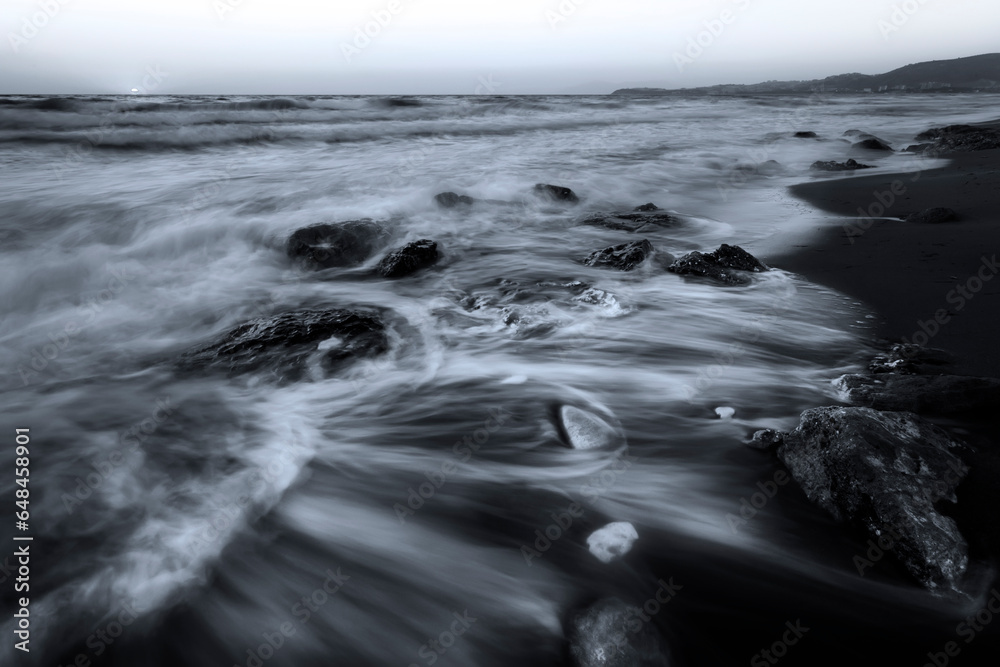 A seascape photographed with a long exposure technique at sunset. Black and white nature landscape.