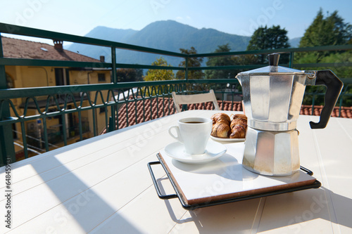 Tablou pe pânză Italian percolator or moka brewer and a cup of freshly brewed coffee on a table on the balcony against the background of the mountains