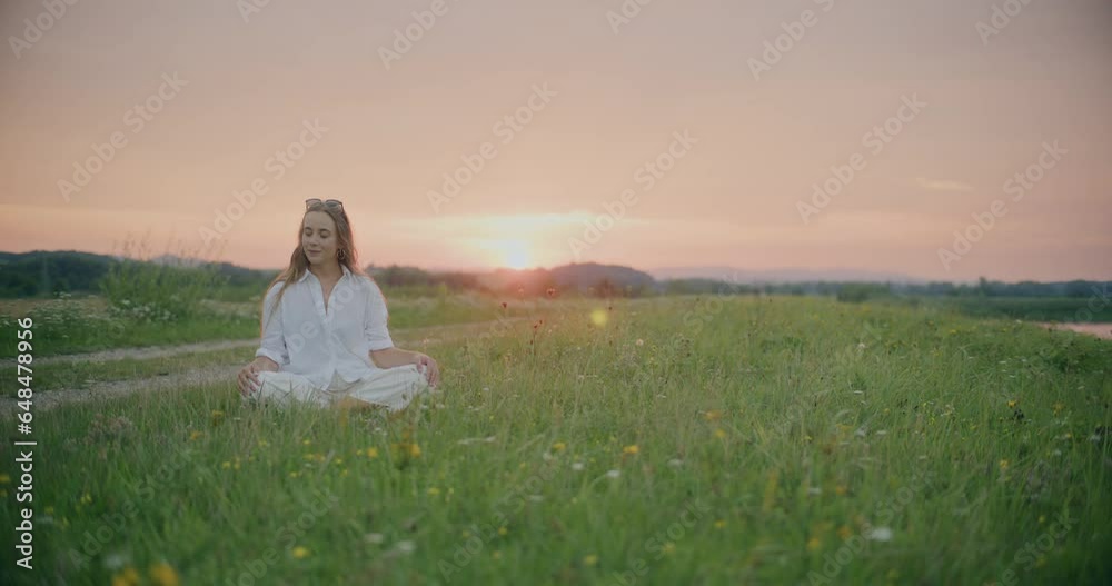 Woman Sitting Cross-Legged In Meadow At Sunset Woman Sitting Cross-Legged In Meadow At Sunset