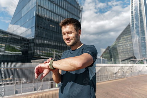 Runner fitness watch uses a mobile app.  A human trainer training in the city. Motivation and mental health of an athlete. An instructor in sportswear. © muse studio