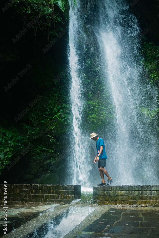 Obraz premium Man Standing on rock in front of high waterfall in mountains in tropical landscape in Jibhi waterfall, Himachl pradesh, india.