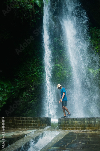 Fototapeta Naklejka Na Ścianę i Meble -  Man Standing on rock in front of high waterfall in mountains in tropical landscape in Jibhi waterfall, Himachl pradesh, india.