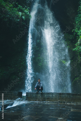 Man sitting on rock in front of high waterfall in mountains in tropical landscape in Jibhi waterfall, Himachl pradesh, india. photo
