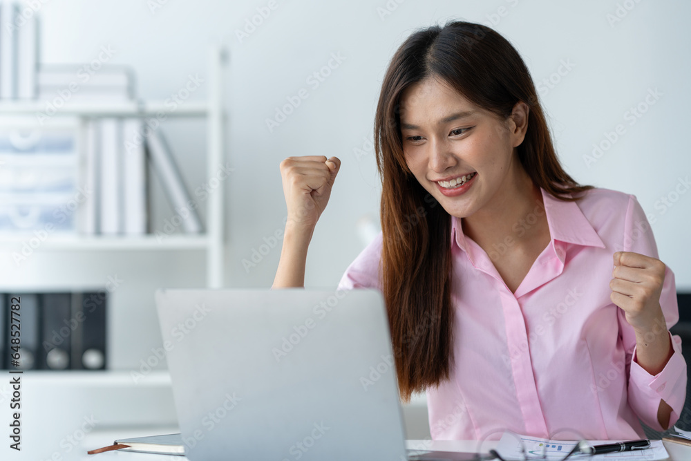 Asian businesswoman raising her hand with a happy expression and looking at her laptop.The businesswoman was delighted to receive an email informing her of her annual bonus. concept of success Asian businesswoman raising her hand with a happy expression and looking at her laptop.The businesswoman was delighted to receive an email informing her of her annual bonus. concept of success