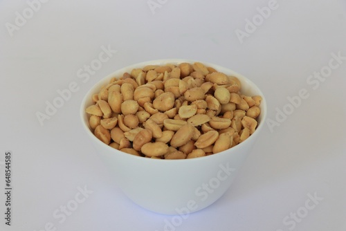 Small bowl of roasted salted peanuts on white background.