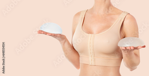 Woman wearing compressing bra after breast augmentation. Holding round implants