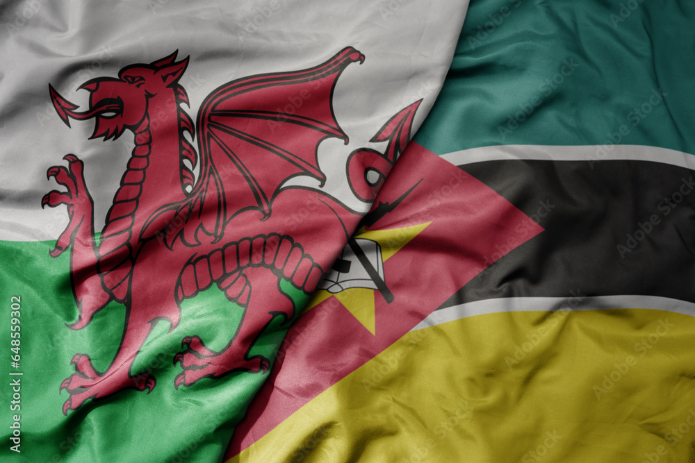 big waving national colorful flag of wales and national flag of mozambique .