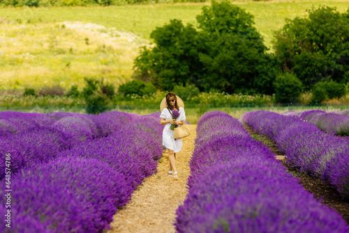 Beautiful lady in a lavender flower field on a summer day. A beautiful woman enjoys a blooming lavender field. Portrait of a young woman in a hat with a bouquet of lavender. 4K, UHD